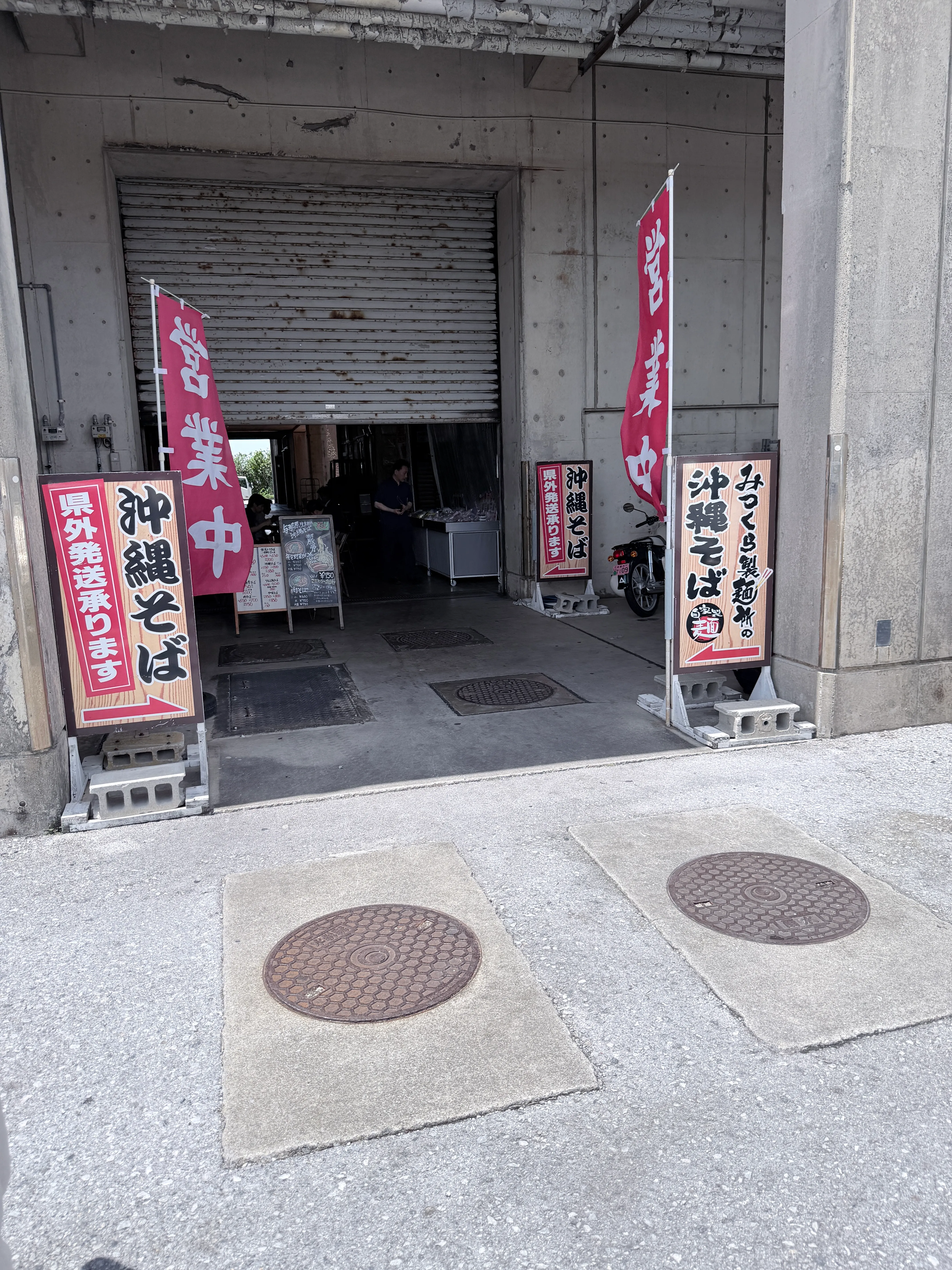 与那原そば本舗 三倉食品中央卸売市場店の店構え。赤いのれんと看板が掲げられている